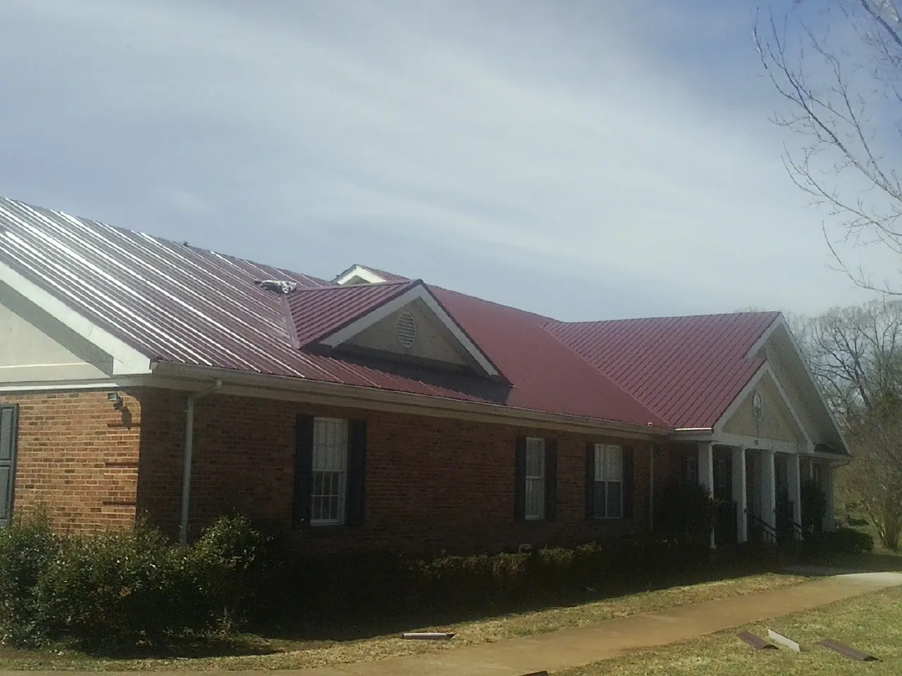 Red metal roof with gabled entries on a long brick building, from a Hail Damage Roof Repair job in Lakeland