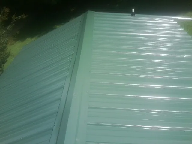 New green metal panels meeting at the ridge of a roof — Flat Roof Repair work by our crew in Lakeland